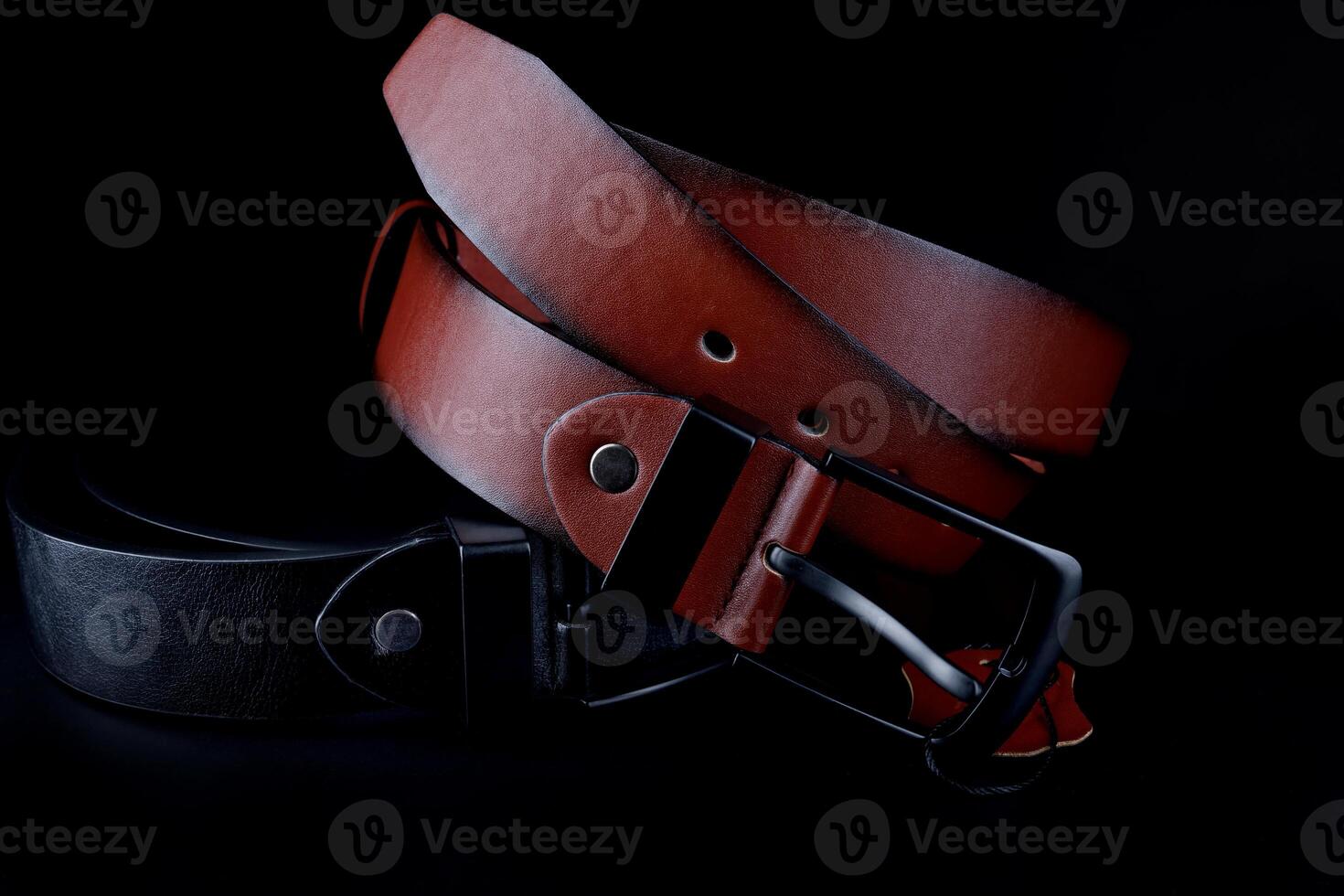 Brown and black leather belts on a black background. photo