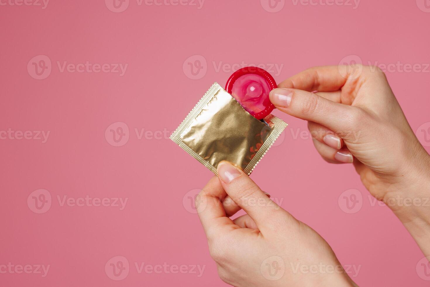 female hands take out a condom from a golden package on a pink background, contraception photo
