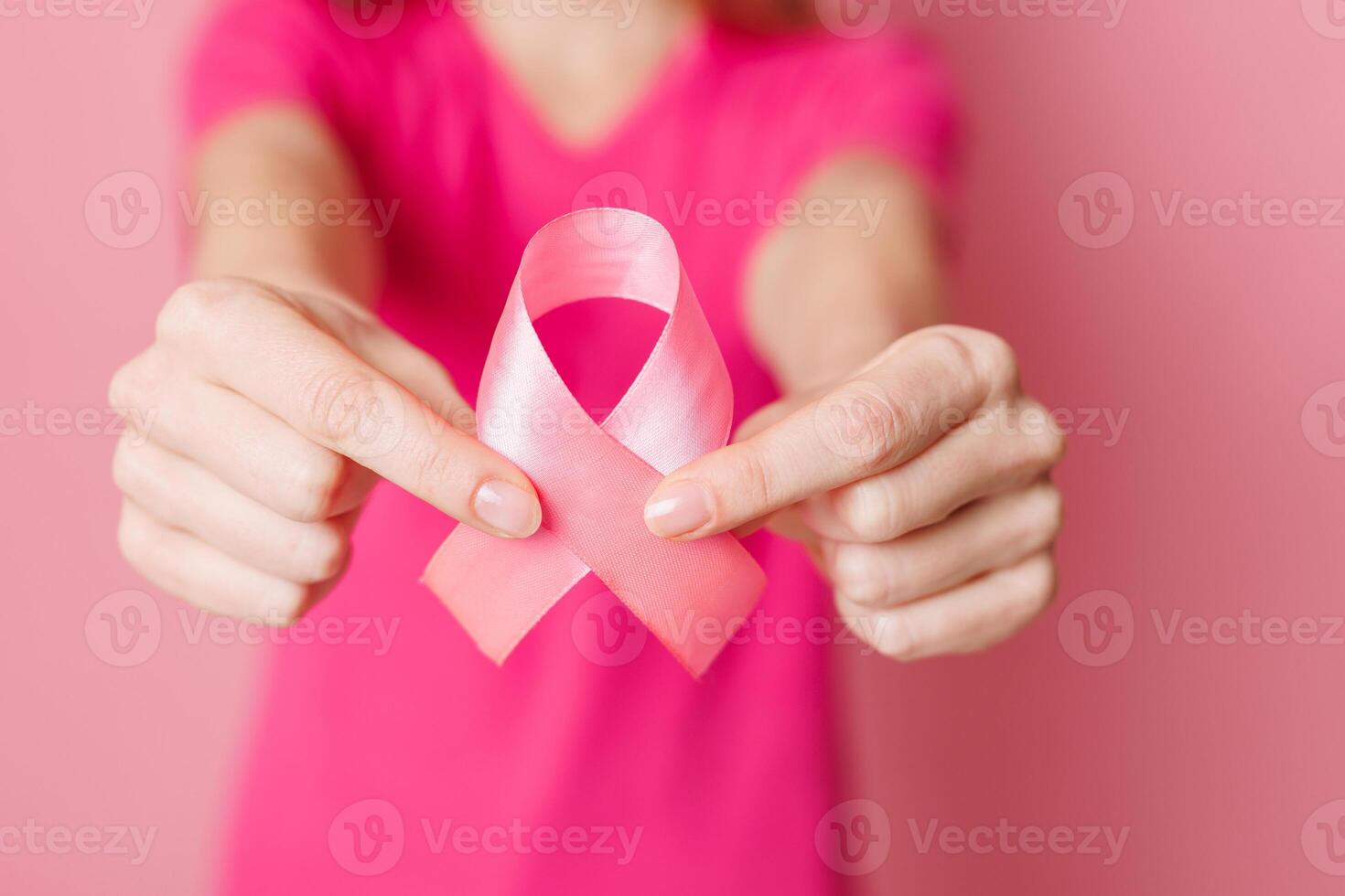 Close up of female hands holding pink ribbon on pink background. Breast cancer awareness concept photo