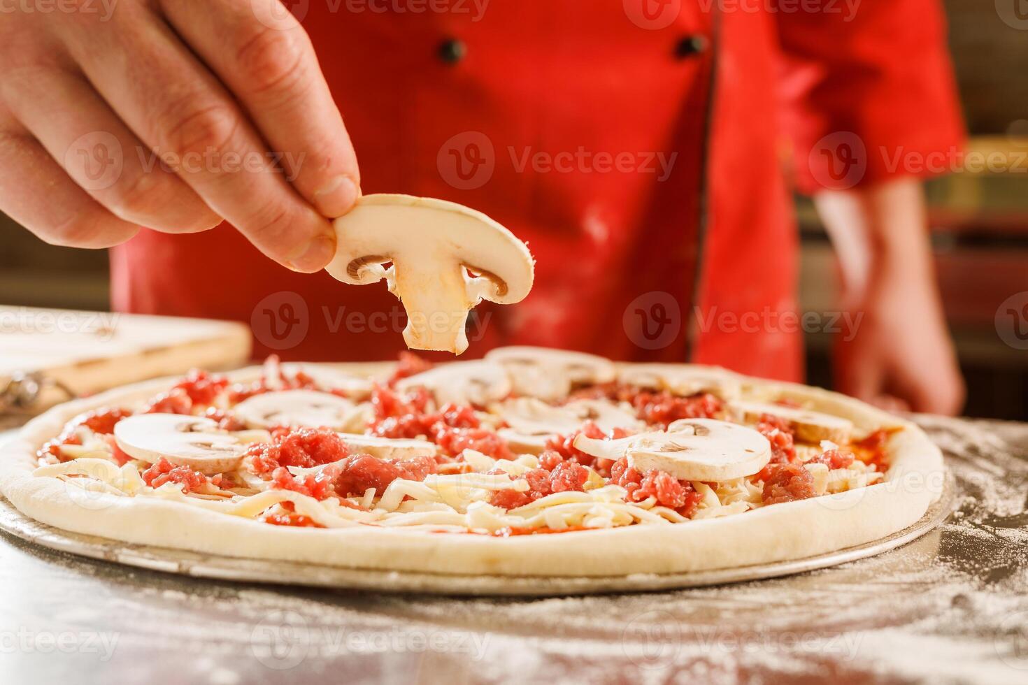 Chef adding mushrooms to uncooked pizza photo