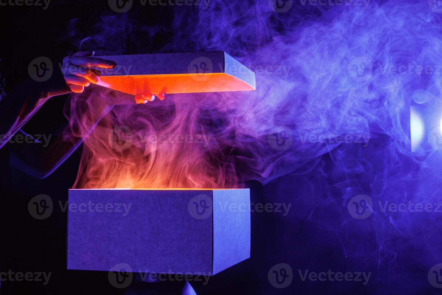 human hands taking out surprise from mysterious box on dark red background surrounded by smoke photo