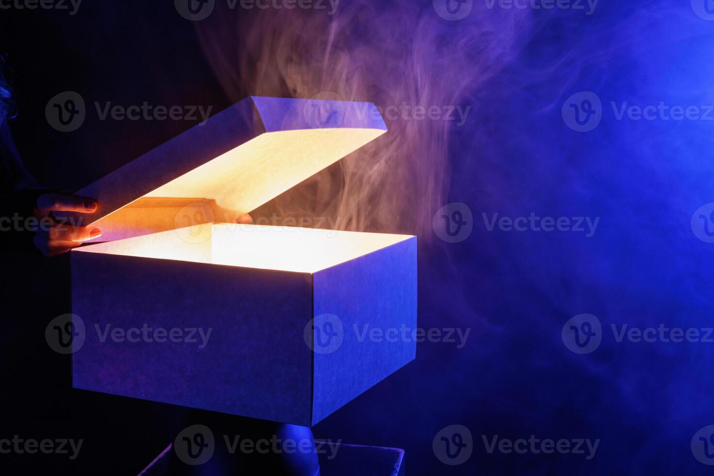 human hands taking out surprise from mysterious box on dark red background surrounded by smoke photo