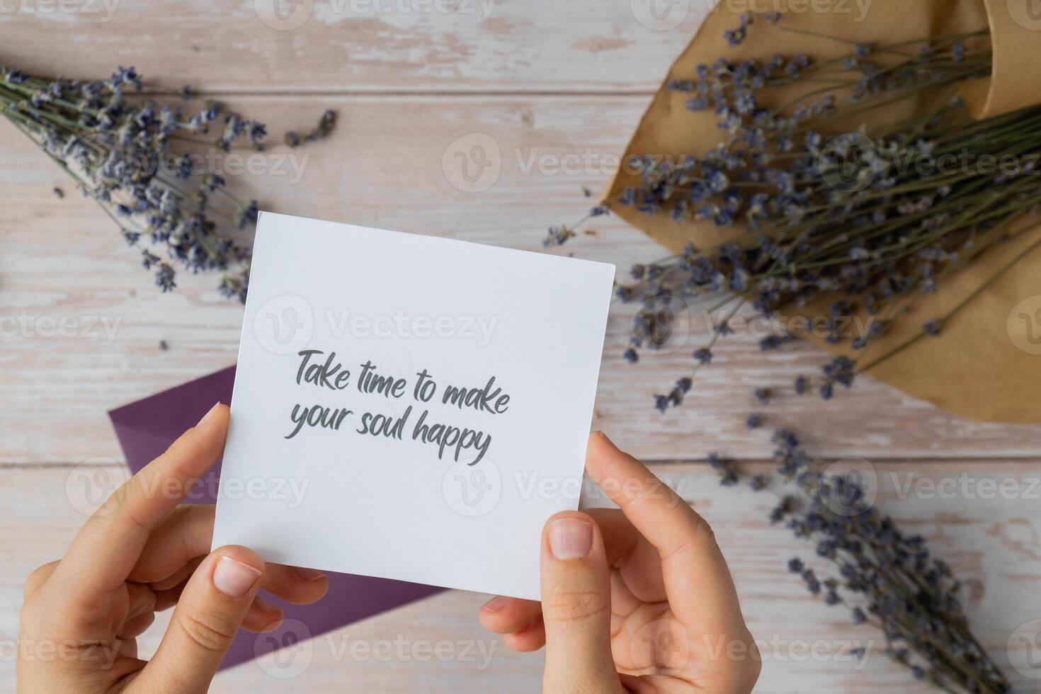 Female hands taking paper card note with text TAKE TIME TO MAKE YOUR SOUL HAPPY from violet envelope. Lavender flower. Top view, flat lay. Concept of mental spiritual health self care wellbeing mindfulness photo