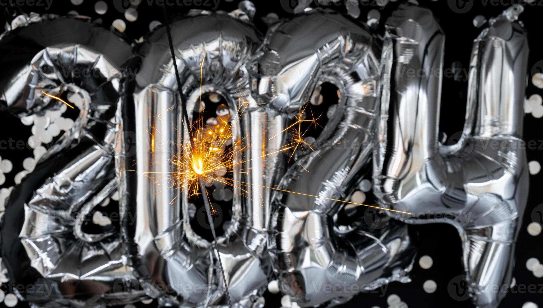 Happy new year 2024 metallic balloons with confetti and sparkler firework Bengal lights on dark black background. Greeting card silver foil balloons numbers Christmas holiday concept. Celebration party congratulation decoration photo