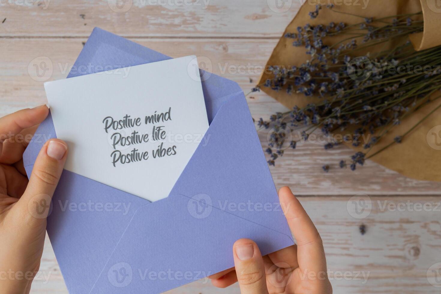 Female hands taking paper card note with text POSITIVE MIND LIFE VIBES from violet envelope. Lavender flower. Top view, flat lay. Concept of mental spiritual health self care wellbeing mindfulness photo