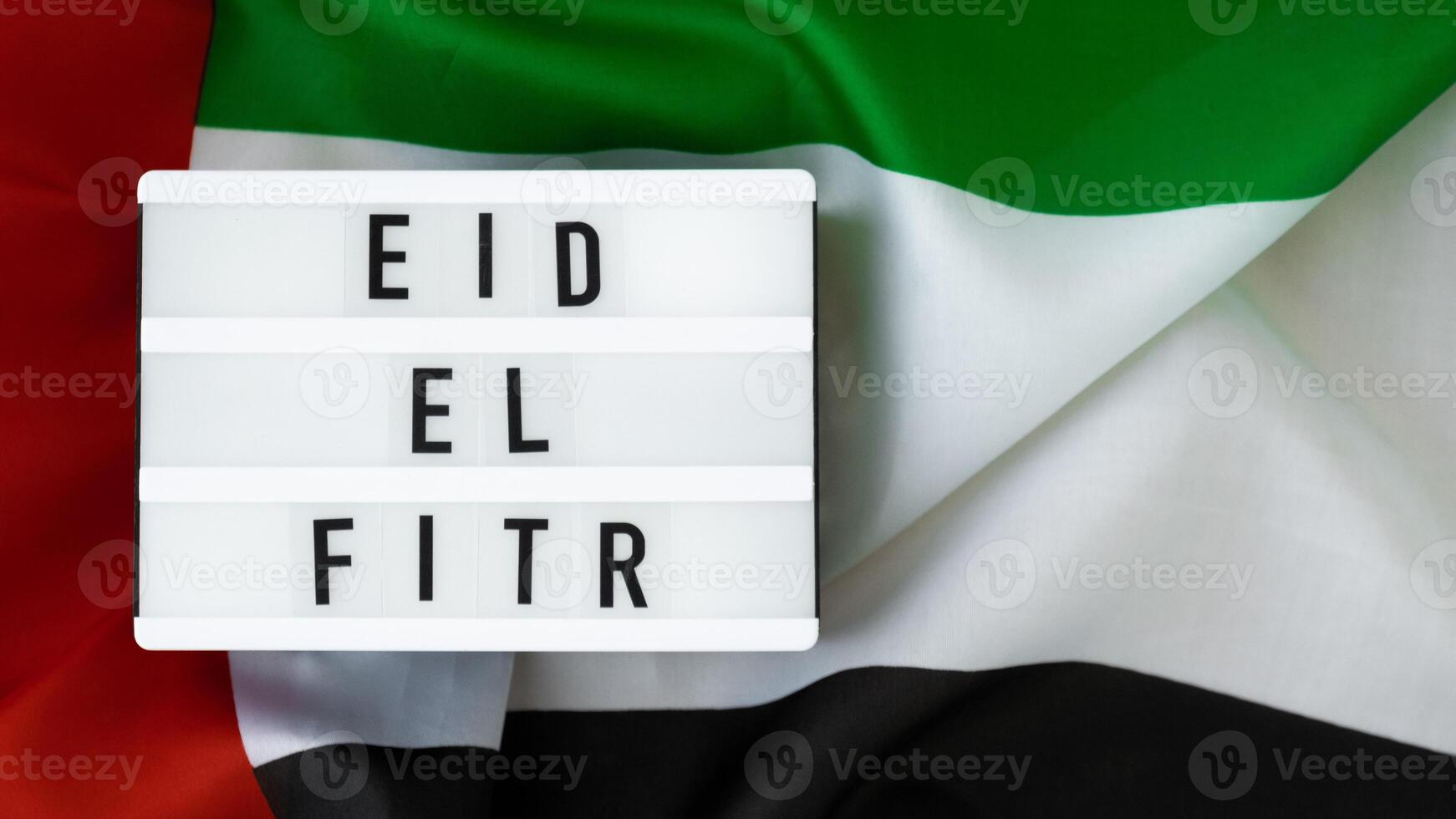 EID EL FITR - Eid Mubarak - Happy Holidays text frame on United Arab Emirates waving flag made from silk material. Public holiday celebration background. The National Flag of UAE. Patriotism Commemoration Day Muslim Ramadan Blessed Holy Month concept photo