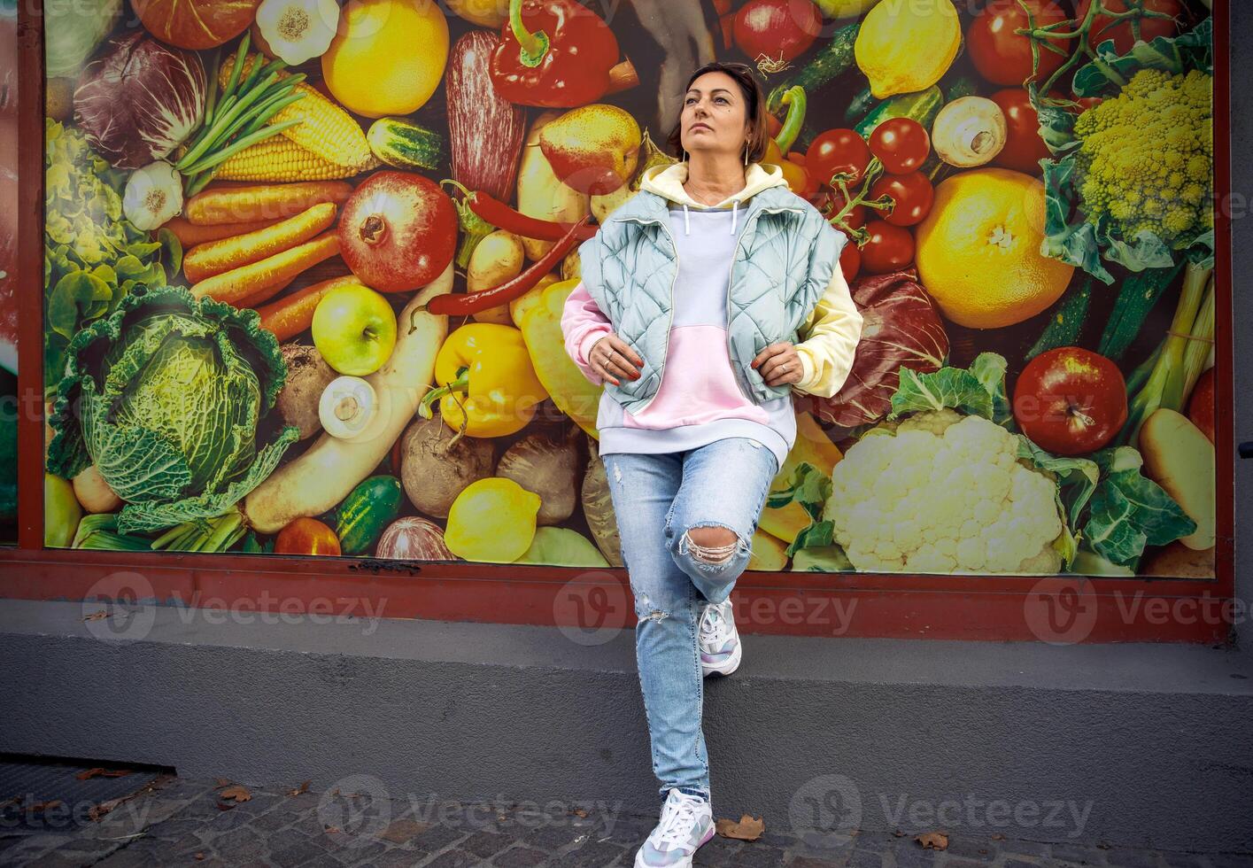 Stylish woman in casual urban outfit relaxing against vibrant vegetable wall mural photo