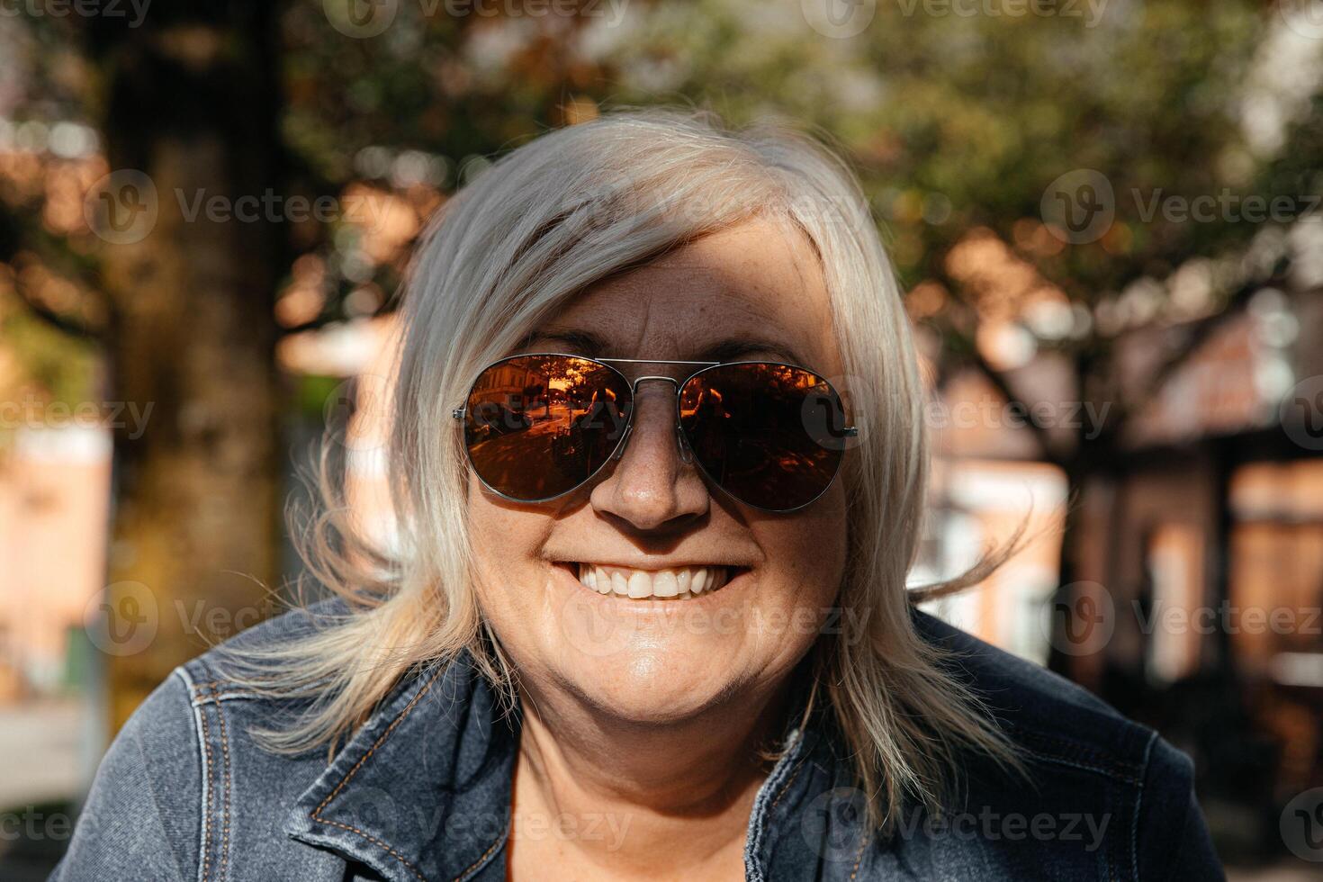 Stylish mature woman with sunglasses smiling outdoors in sunlight photo