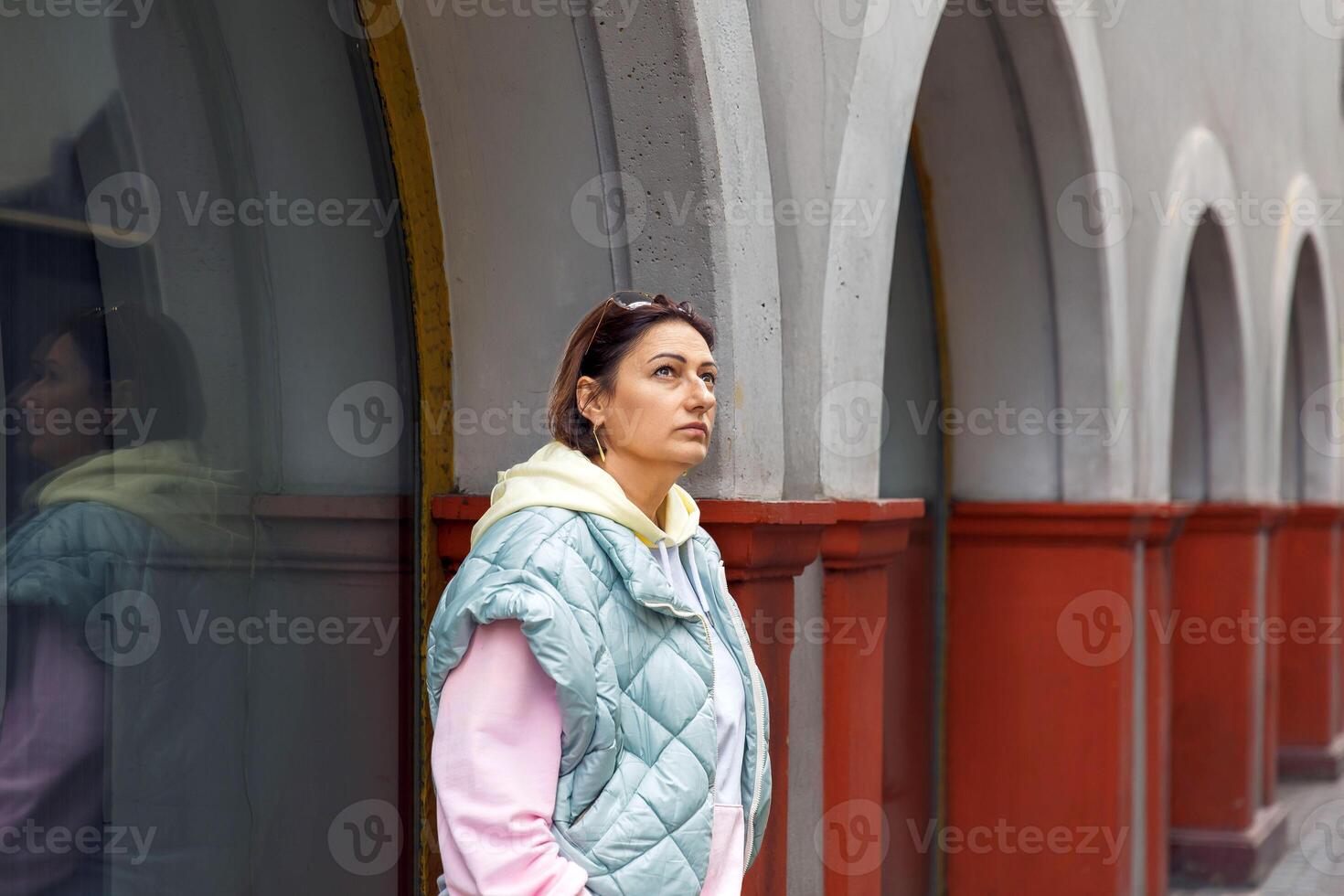 Woman in quilted jacket strolling by arched architecture photo