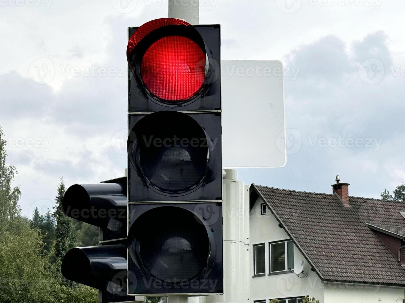 Red traffic light at intersection on cloudy day with empty street in background photo