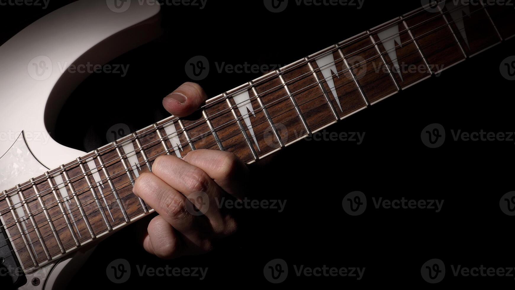 Guitarist Playing Guitar In Studio. Low key of man hand play white electric guitar for songs and cover music or skill practice. Close up of musician playing guitars instrument against black background photo