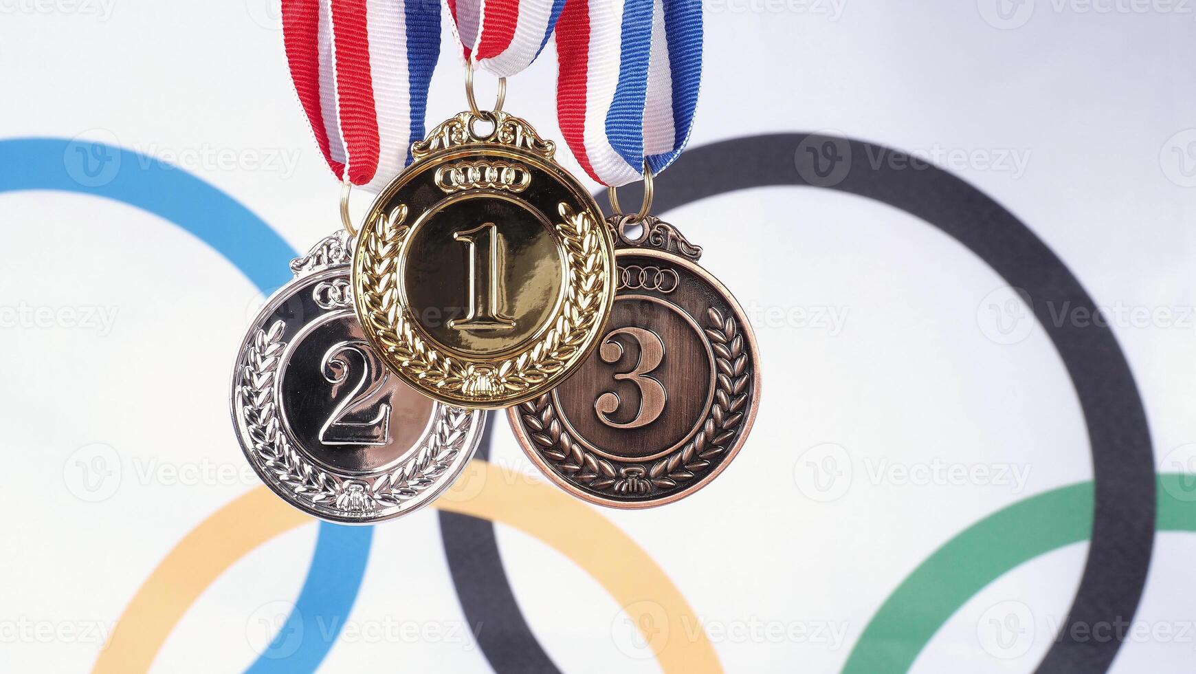 Close up of gold silver and bronze mockup trophy medals with ribbon against olympic flag mockup and white background for national or olympic sport international competition. Award and victory concept. photo