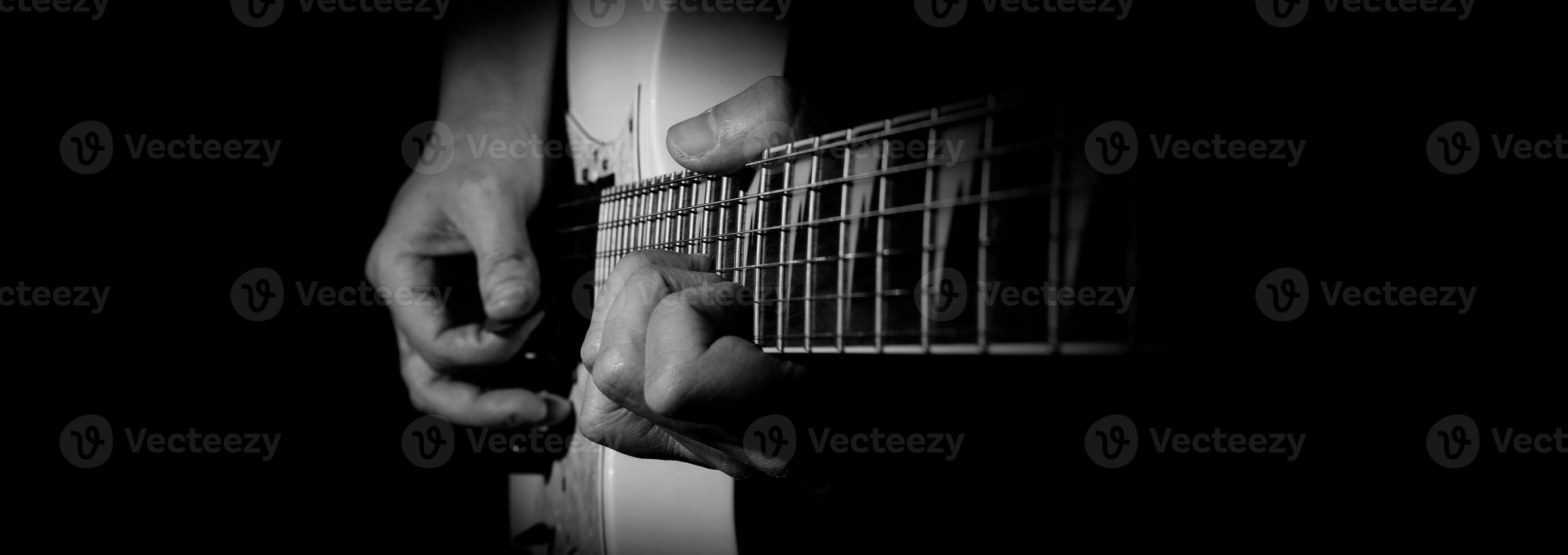 Guitarist Playing Guitar In Studio. Low key of man hand play white electric guitar for songs and cover music or skill practice. Close up of musician playing guitars instrument against black background photo