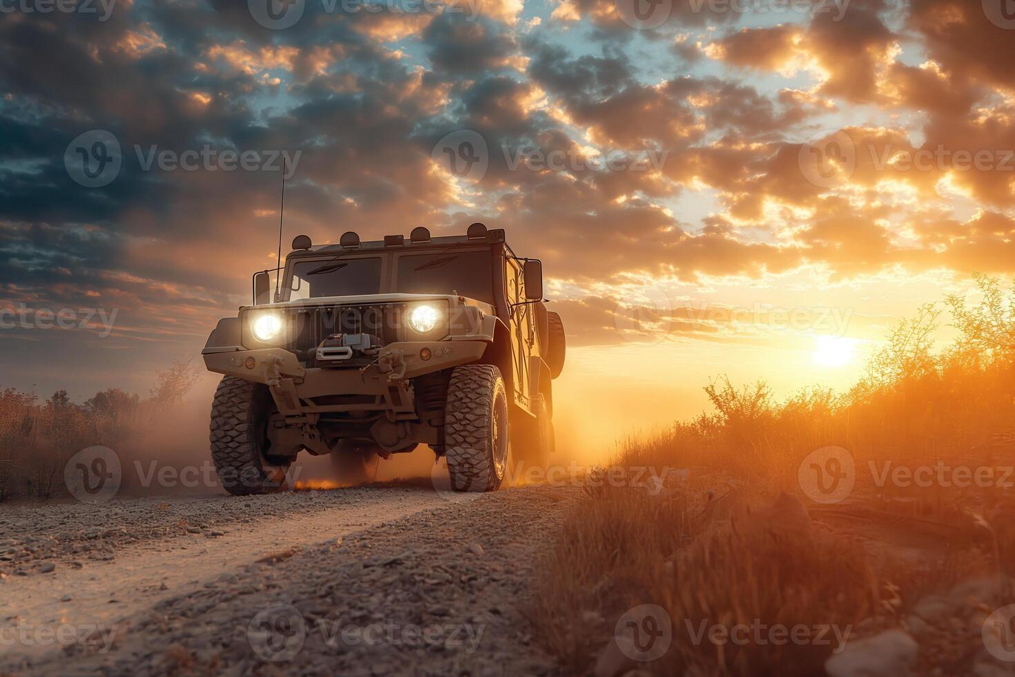 Military vehicle driving on a dirt road during sunse photo