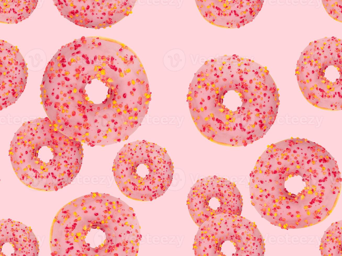 Seamless pattern of pink frosted donuts topped with colorful sprinkles on a pastel pink background. Stock photo