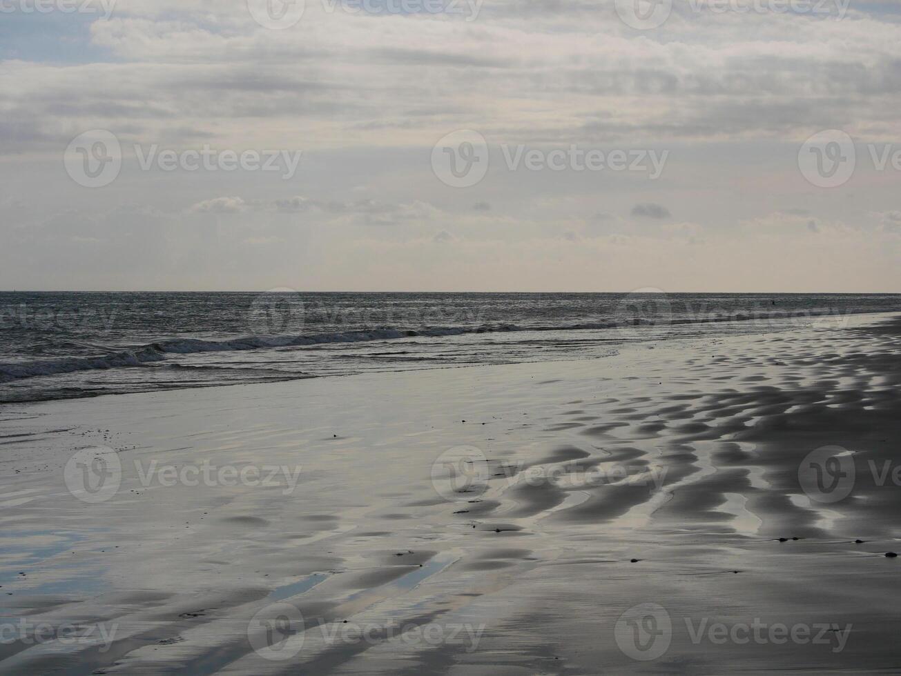 Seashore in sunlight with reflections on wet sand photo