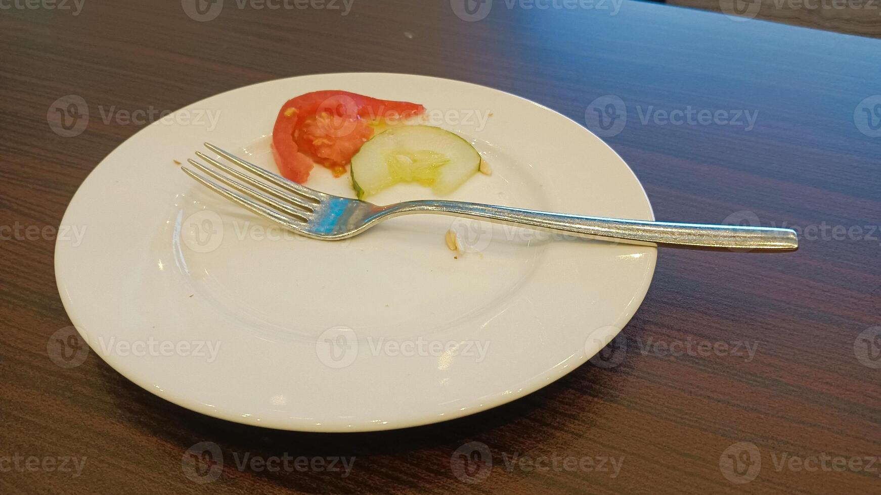 Empty plate with a fork, tomato and cucumber slices on a wooden table. photo