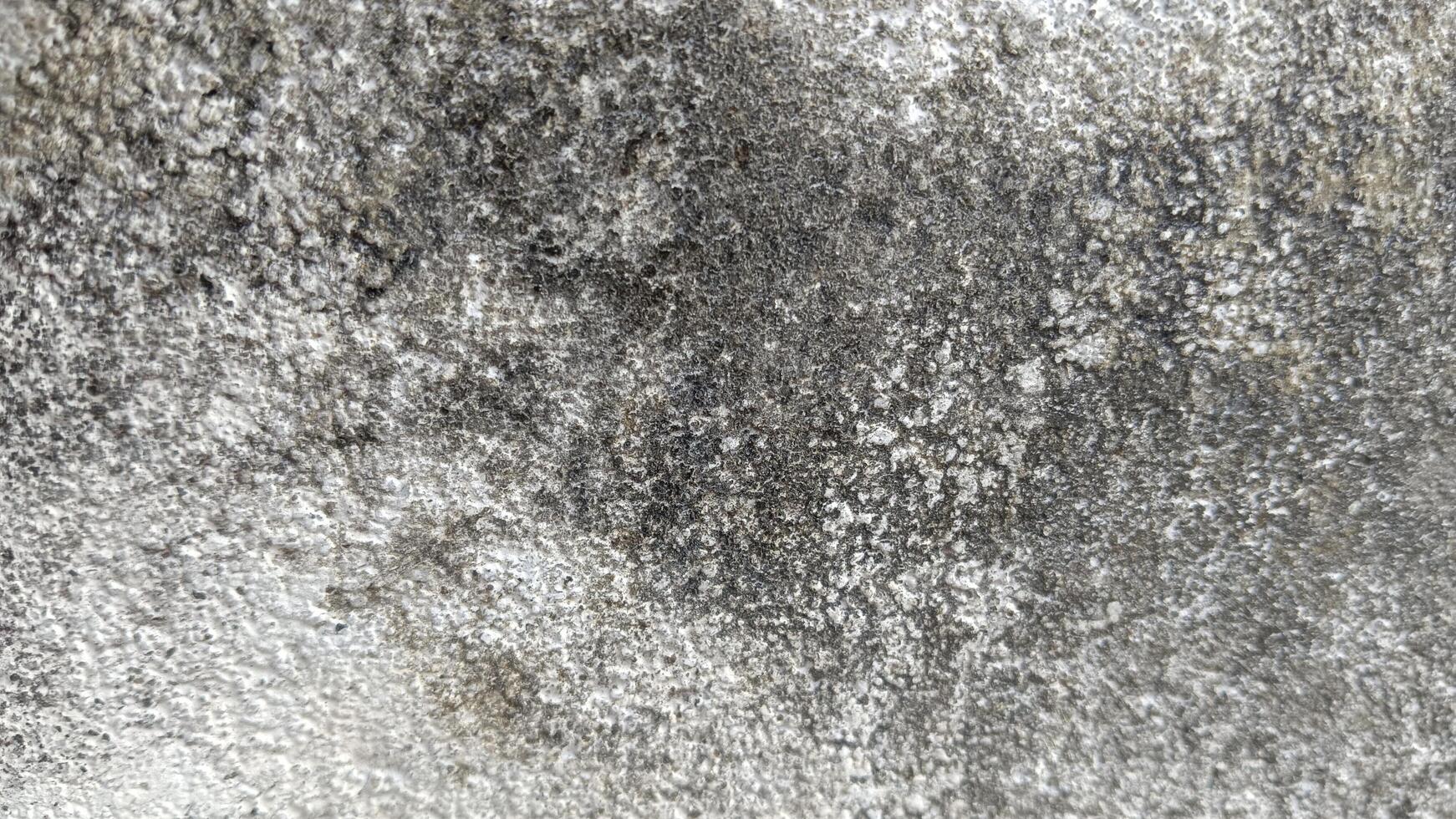 Close-up of a rough, weathered concrete wall with a mottled, uneven texture. photo