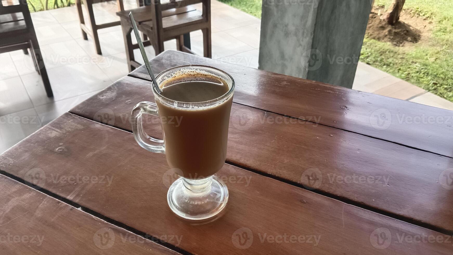 A glass mug of coffee on a wooden table in a cafe. photo