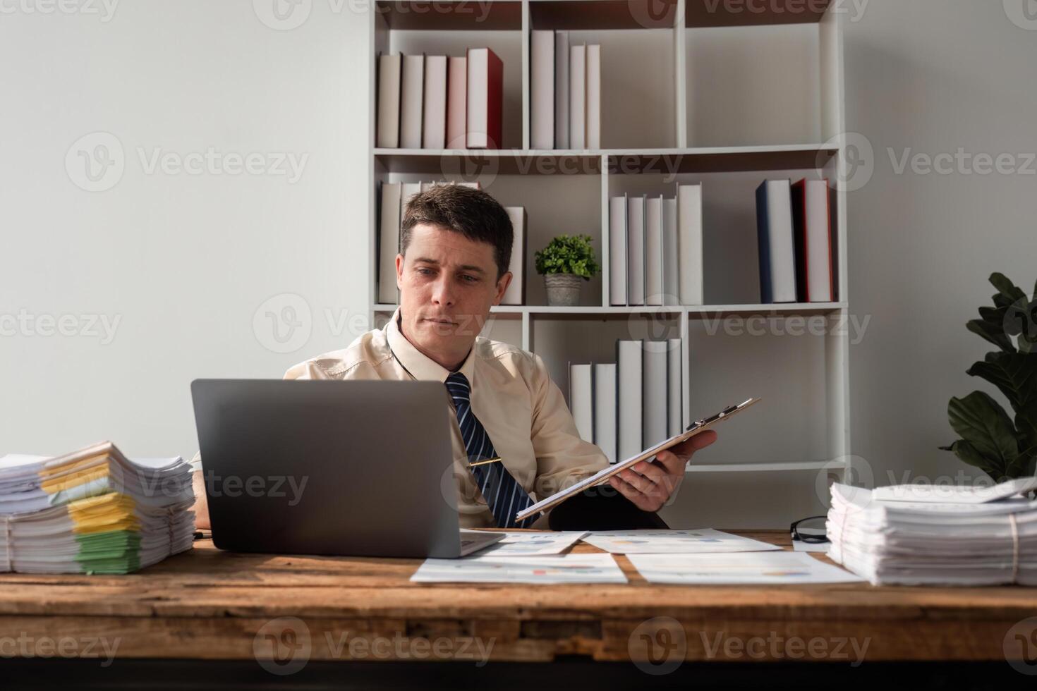 Young Businessman Working in Modern Office with Laptop and Documents, Focused on Tasks, Professional Workspace photo