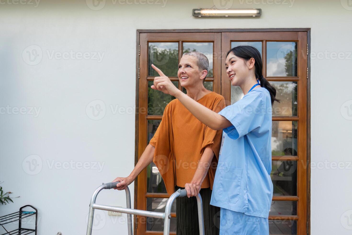Elderly Woman and Caregiver Enjoy a Walk in the Garden Outside Their Home on a Sunny Day photo