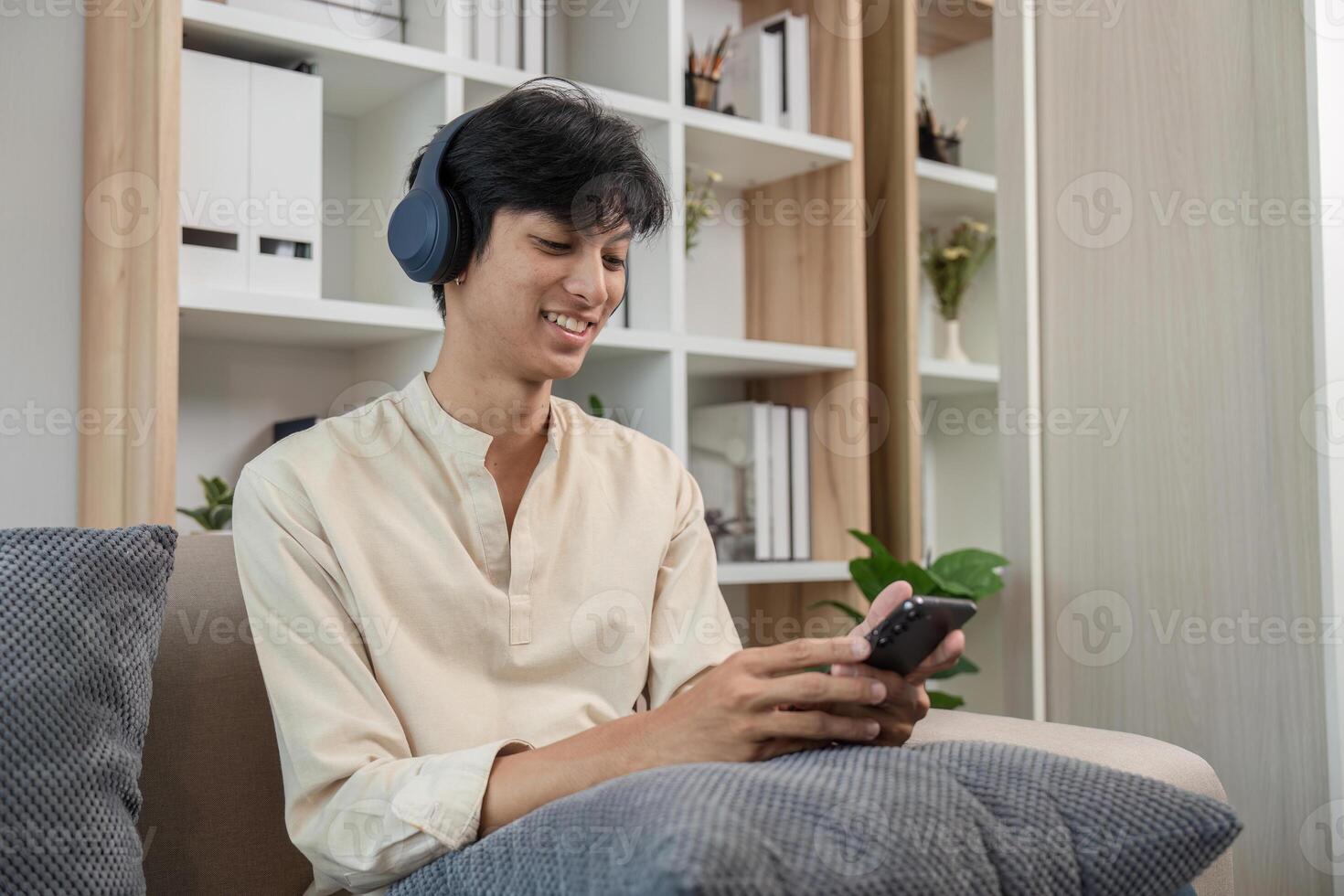 Young Man Relaxing in Modern Room While Playing on Phone and Wearing Headphones photo