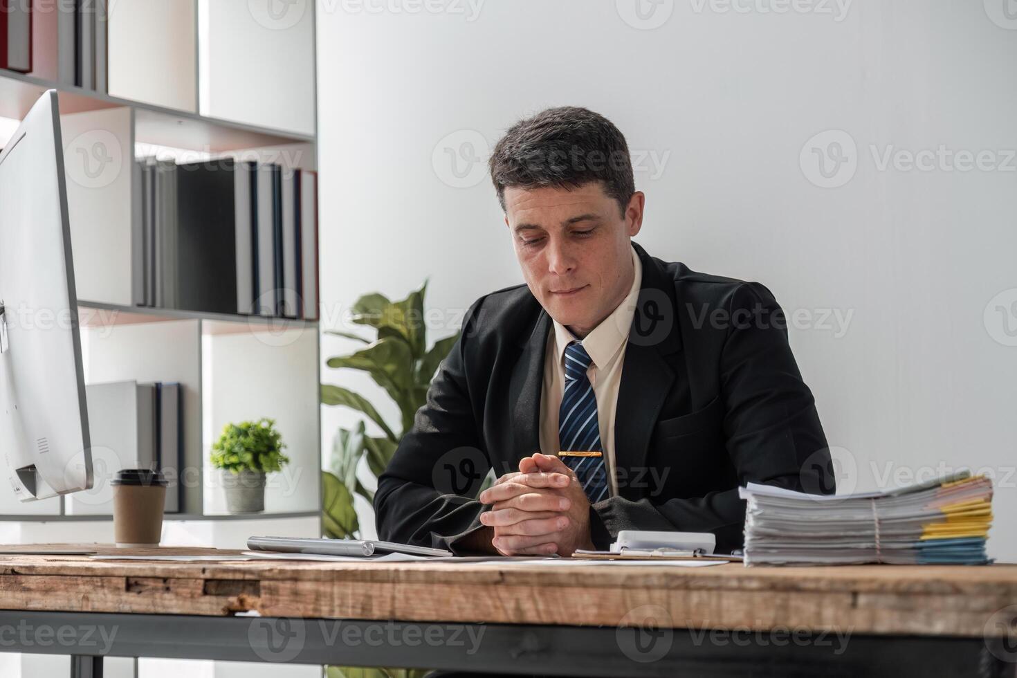 Young Businessman Deep in Thought at Modern Office Desk with Documents and Computer, Focused on Serious Work photo