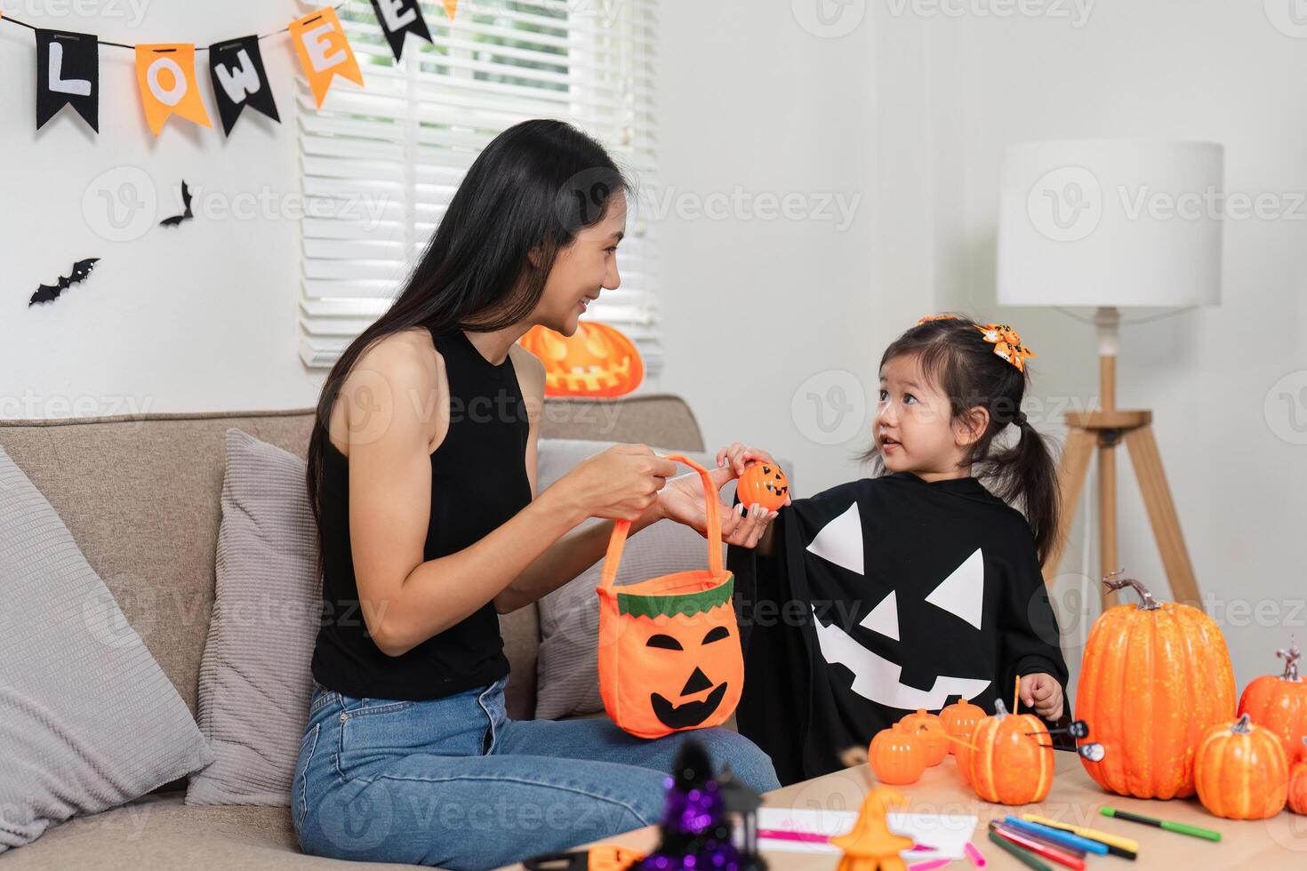 Mother and Daughter Enjoying Halloween Activities Together at Home, Decorating with Pumpkins and Costumes photo