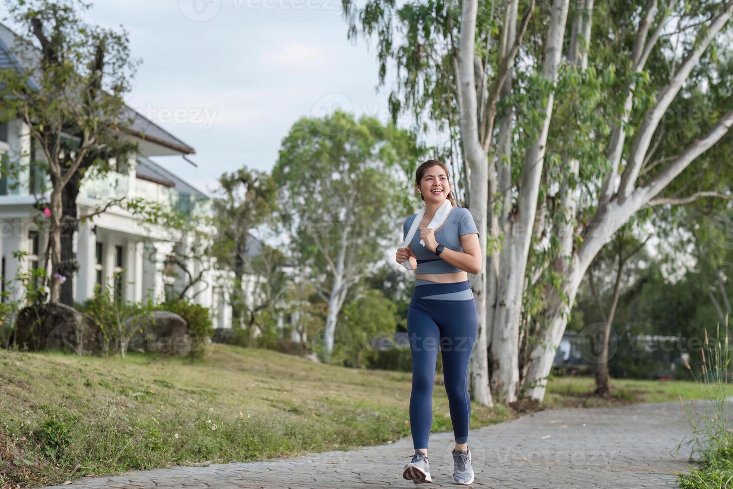 Woman Enjoying a Refreshing Jog in the Park on a Sunny Day with Greenery and Houses in the Background photo