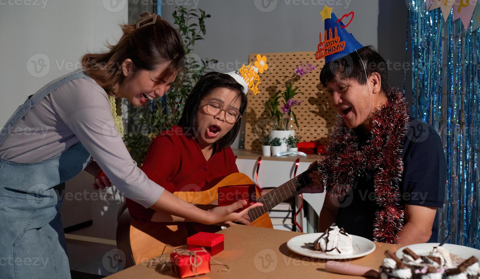 A man in a red shirt is playing a guitar while a woman and a child look on photo