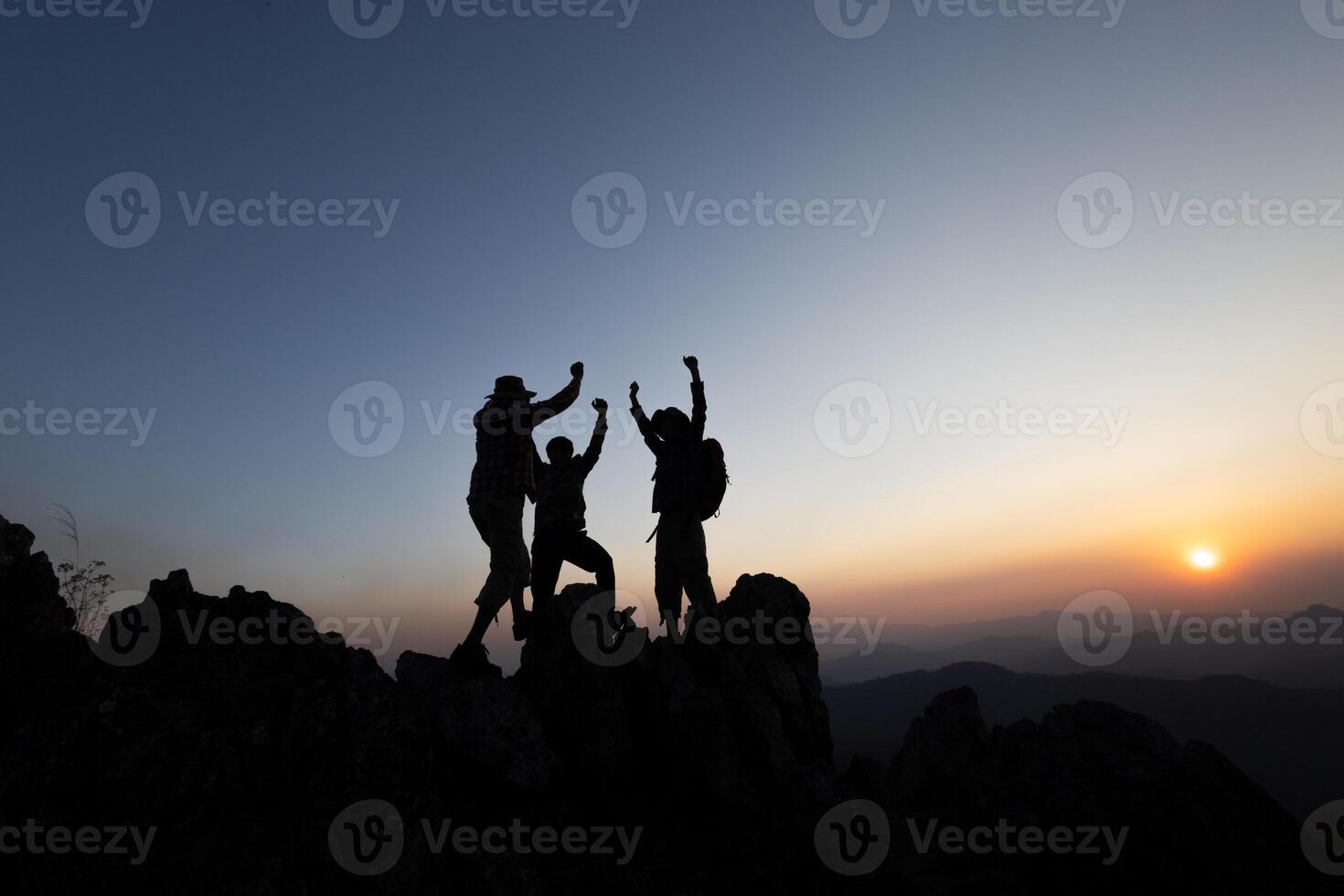 Silhouette of Together overcoming obstacles with three people holding hands up in the air on mountain top. climbing team work success business concept. growth and success. photo