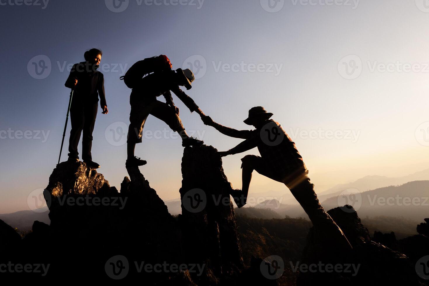 Silhouette of Hikers climbing up mountain cliff. Climbing group helping each other while climbing up in sunset. Concept of help and teamwork. photo