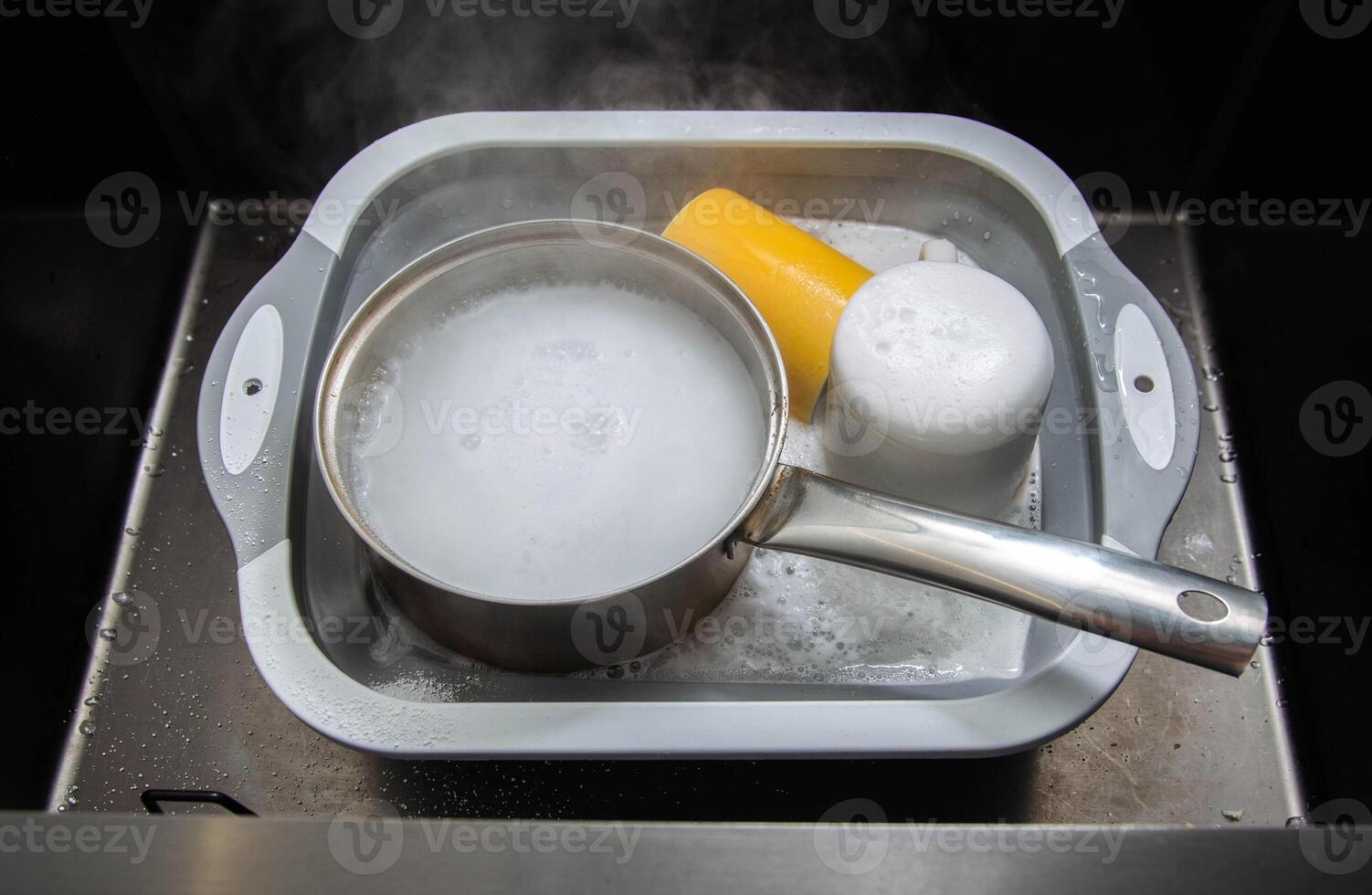 Dirty dishes in a sink basin with hot water and foam from an environmental oxygen cleaner. A modern product for removing dirt and stains. photo