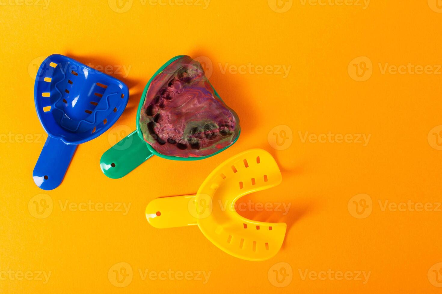Multi-colored dental spoons for taking an impression of the dental jaw on a orange background. Making an impression of the jaw for braces and dental prosthetics, close-up. Copy space for text photo