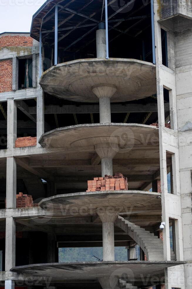 An unfinished concrete building structure symbolizes urban development challenges and opportunities, with stacks of bricks awaiting construction completion photo