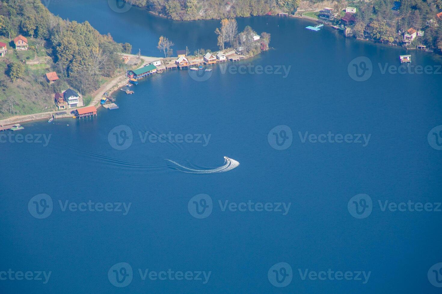 Aerial view of a speedboat making waves on a serene lake surrounded by lush greenery, perfect for a summer vacation concept photo