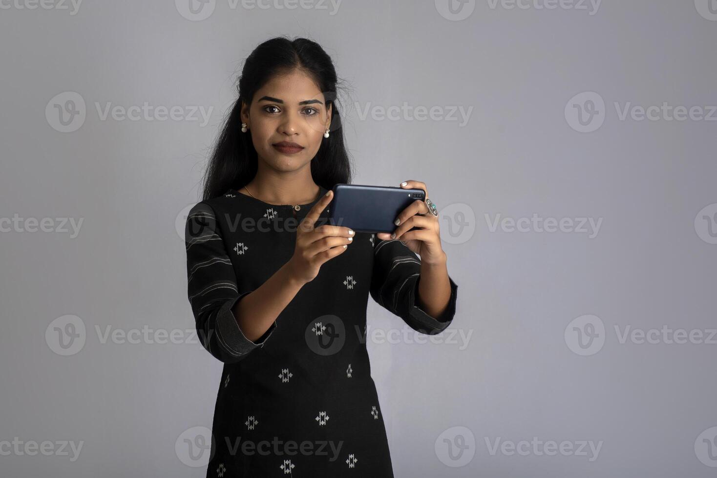 Young Indian girl using a mobile phone or smartphone on gray background photo