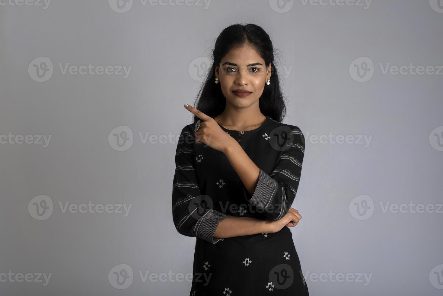 Young smiling girl pointing fingers to copy space on a grey background photo