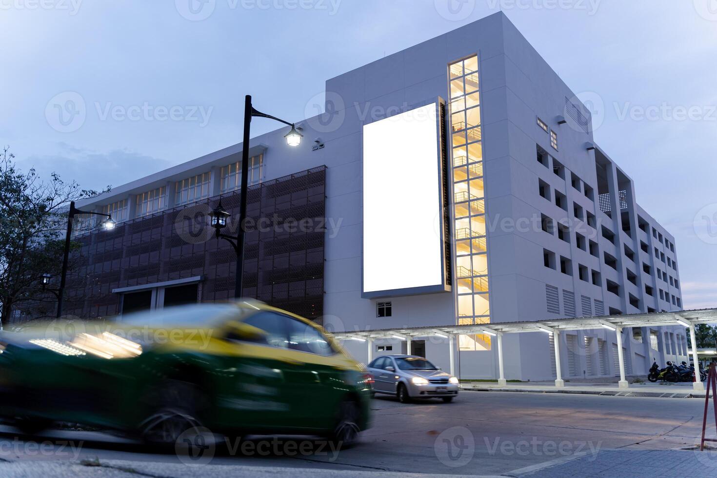Blank billboard and high rise business building at night time. A bright blank billboard stands out from the surrounding downtown area in the evening as a copy space photo