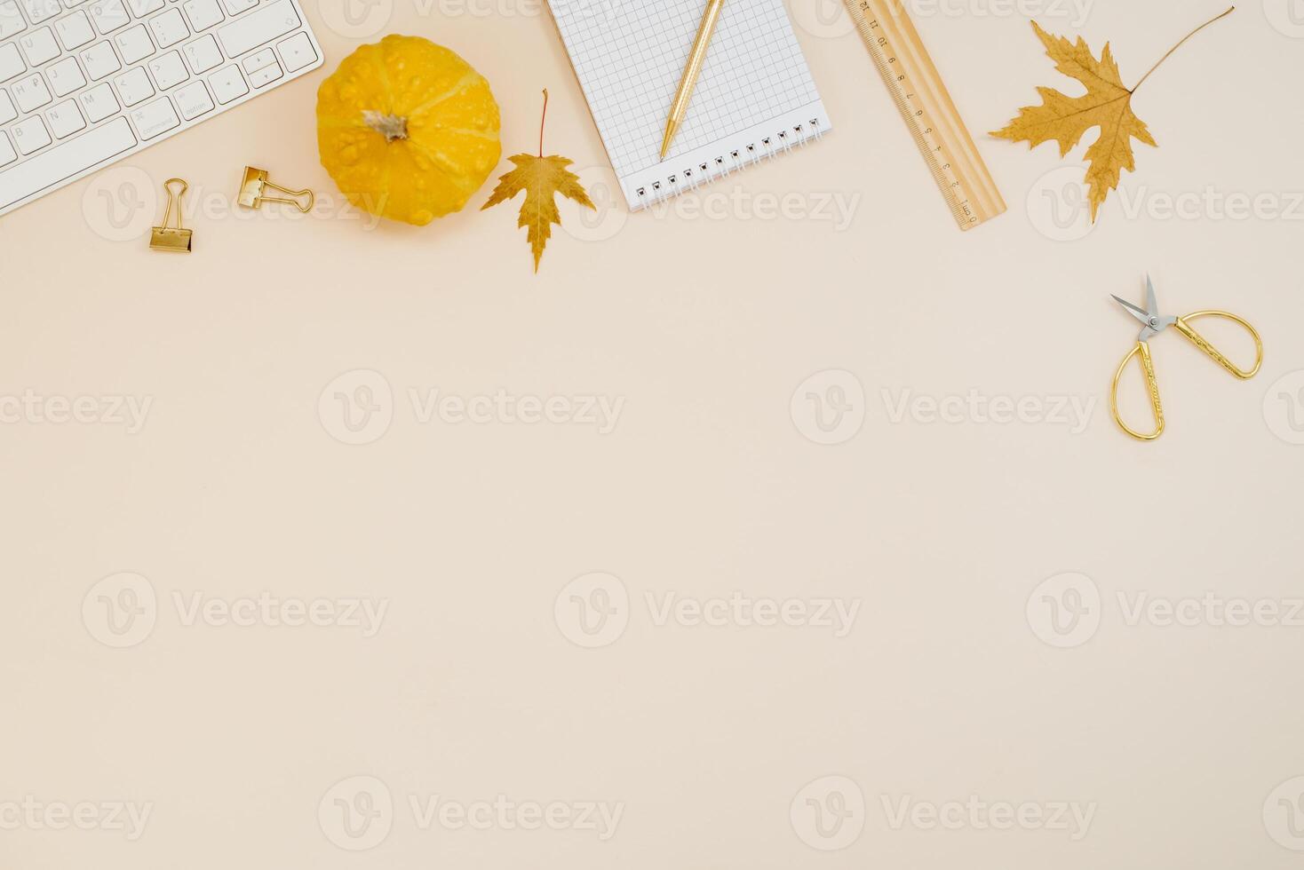 Flat lay home office desk. Freelancer or blogger workplace with computer, yellow pumpkins, fallen leaves, scissors, notepad, ruler and pen on a light beige background with copy space photo