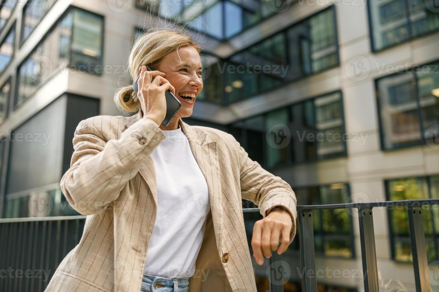 Smiling woman freelancer is standing on modern building background and looking at side photo
