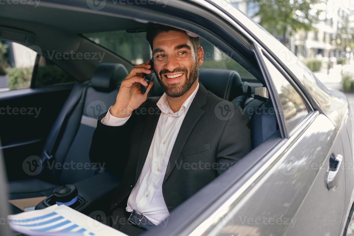 Smiling businessman talking phone with client while sitting on car backseats photo
