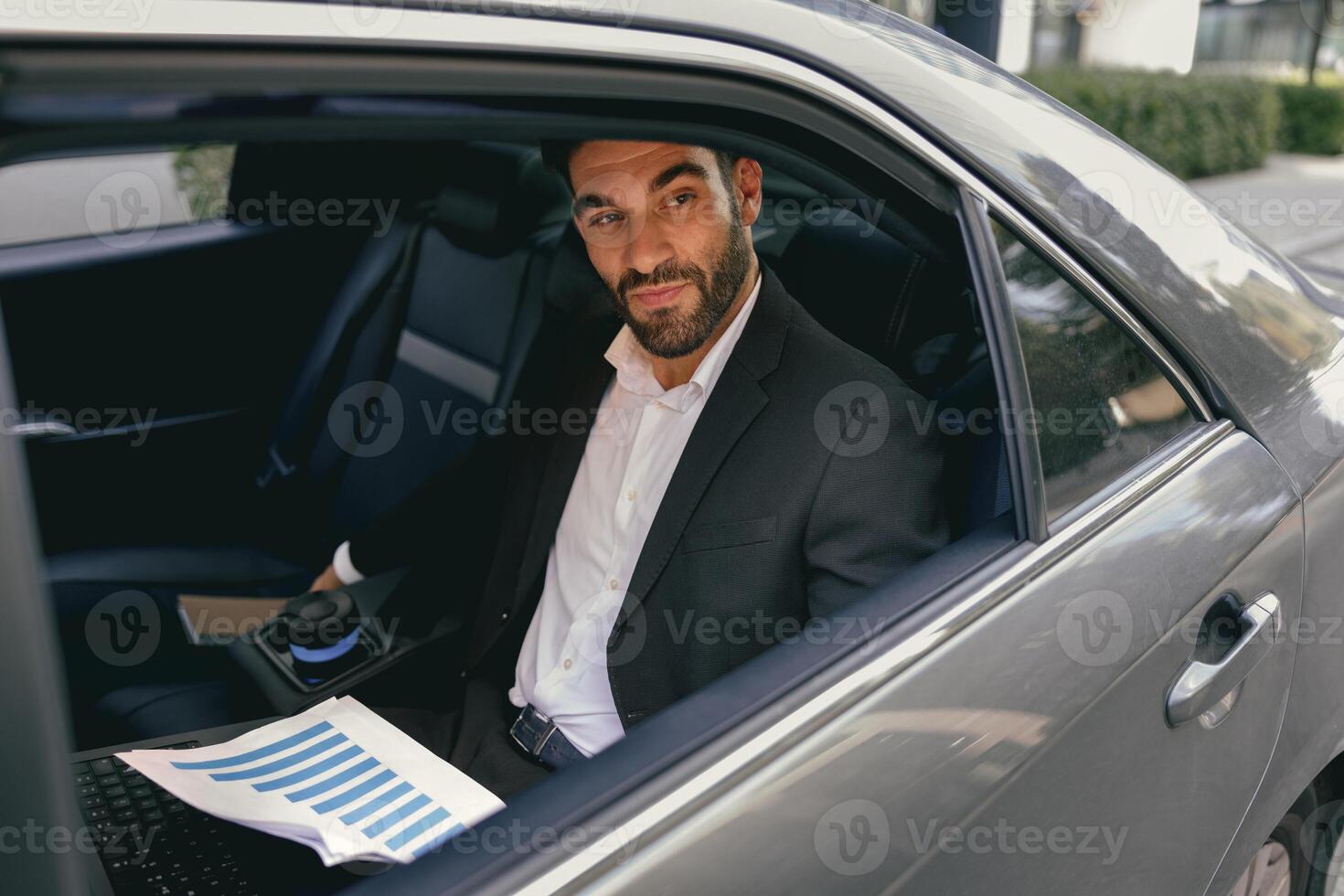 Confidence businessman sitting on car backseat and working with documents and use laptop photo