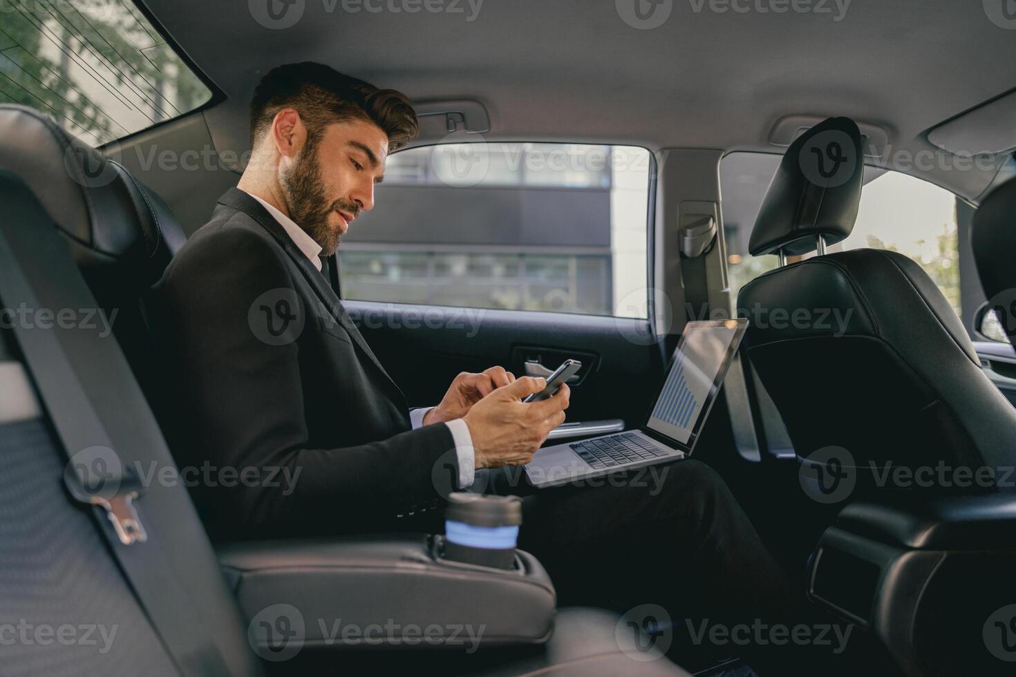 Busy male analyst working on laptop and use mobile phone while going to airport by car photo