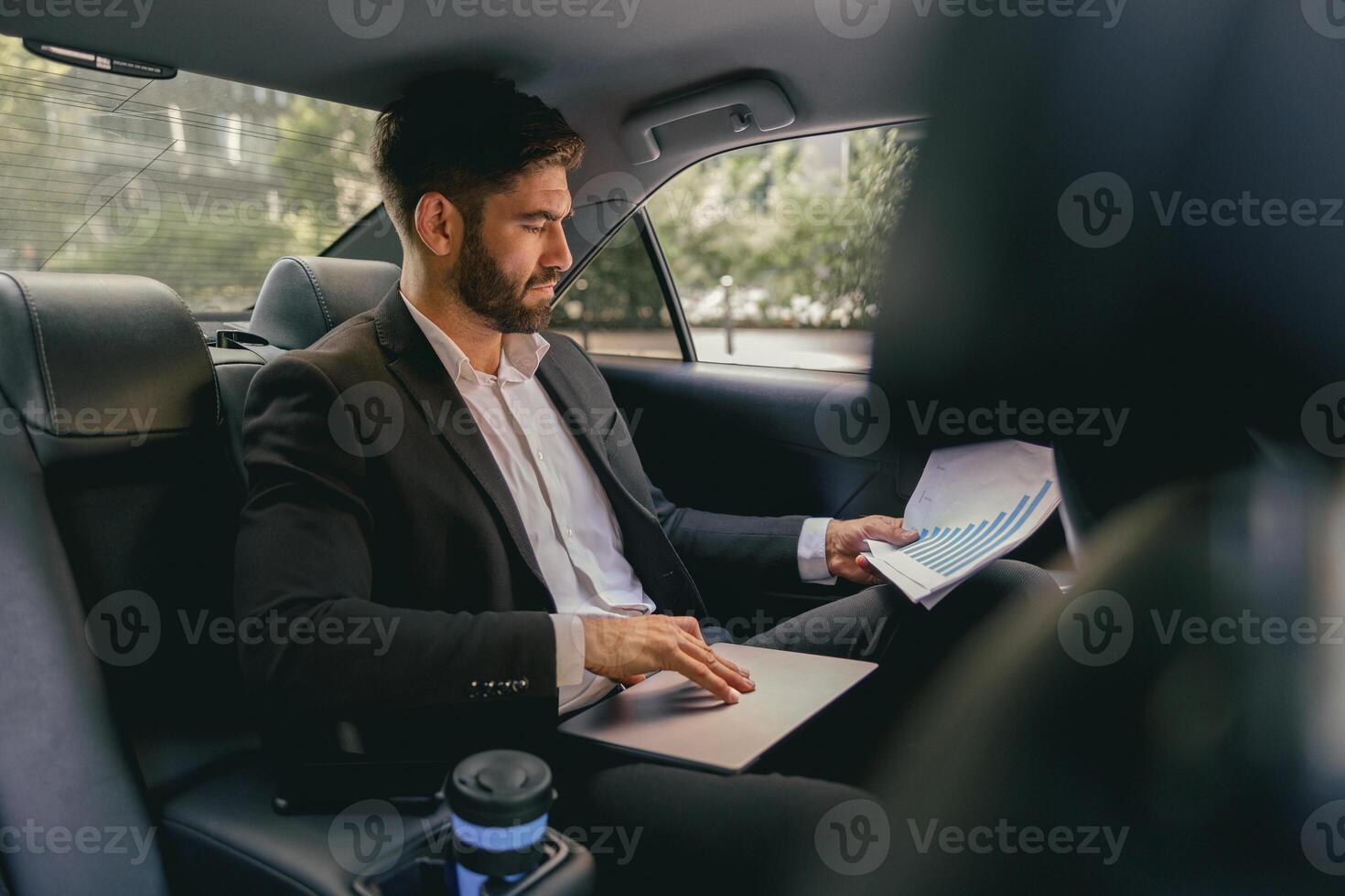 Male entrepreneur sitting on car backseat and working with documents while going to office photo