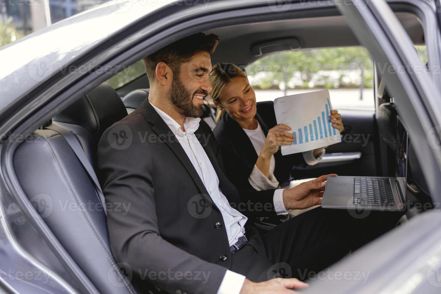 Smiling business analysts have online meeting using laptop while sitting in car back seats photo