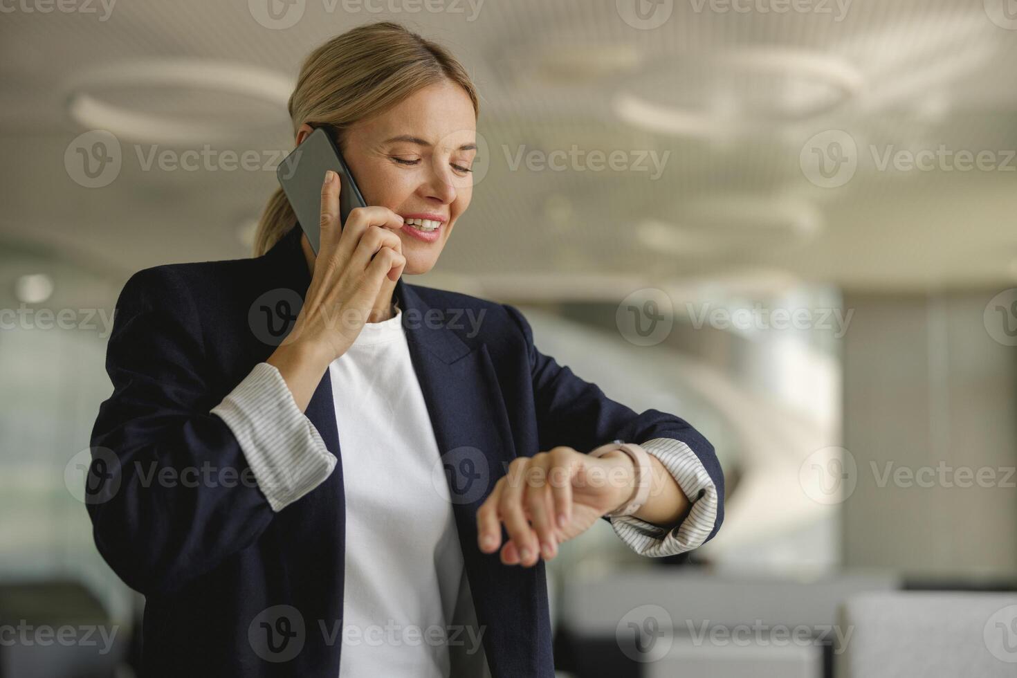 Female sales manager looking at wristwatch to checking time while having a phone call with client photo