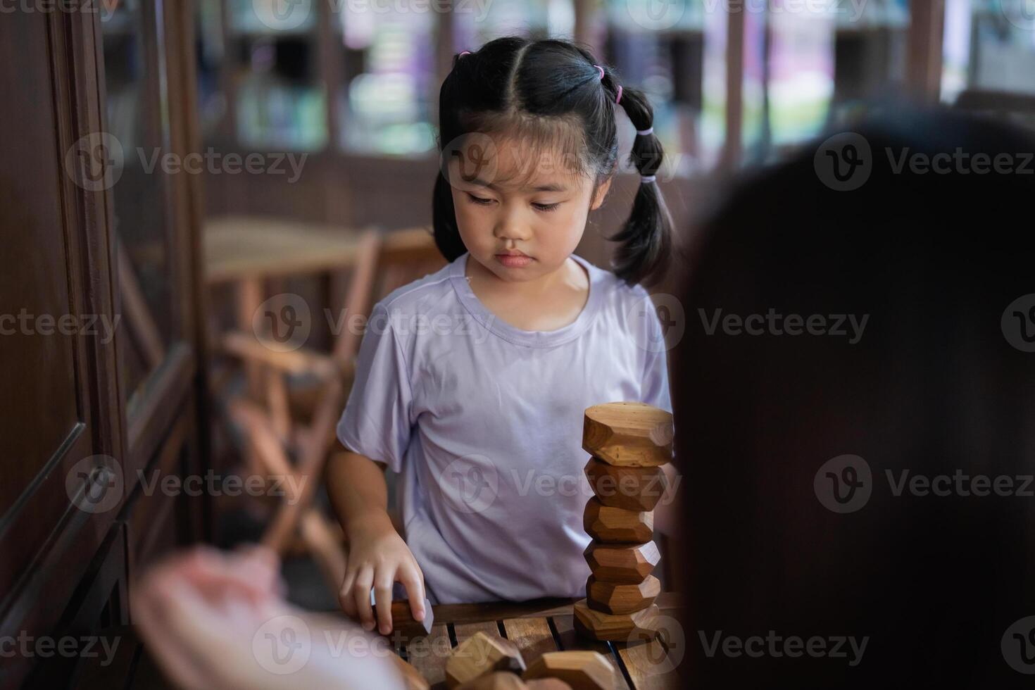 Asian young girl is playing with wooden blocks. She is wearing a purple shirt and has her hair in pigtails photo