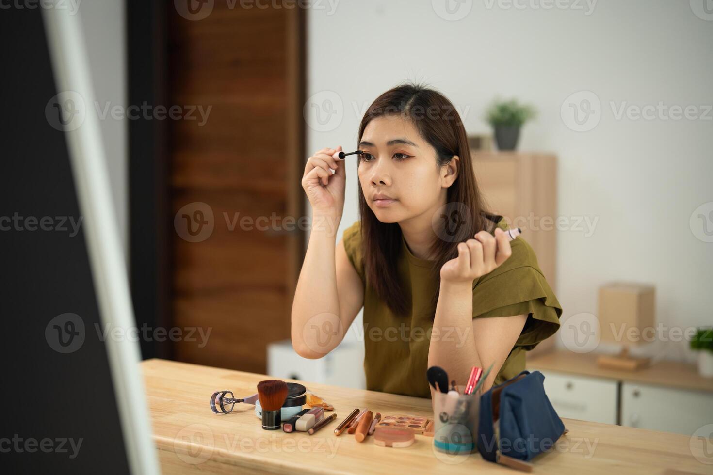 Asian woman is applying makeup in front of a mirror. She is using a brush to apply eyeliner photo