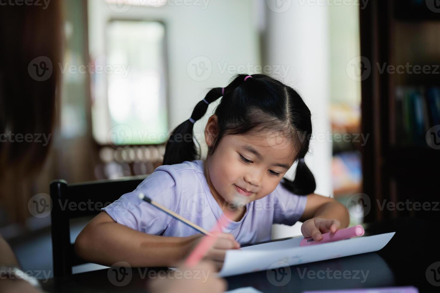 Asian young girl is sitting at a table with a pencil and a piece of paper. She is writing something down and she is focused on her task photo
